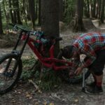Een fietspomp geschikt voor Presta ventielen naast een fiets met een lege band in de natuur.
